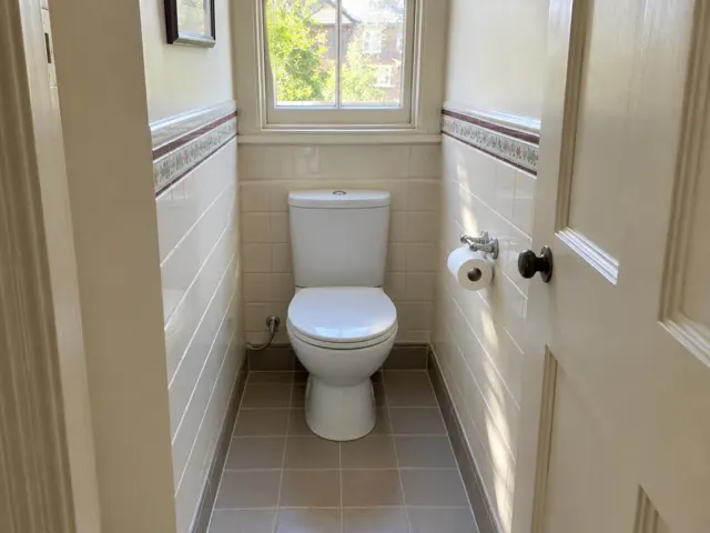 Clean white toilet in a small tiled bathroom with a window and cream walls in Lindfield