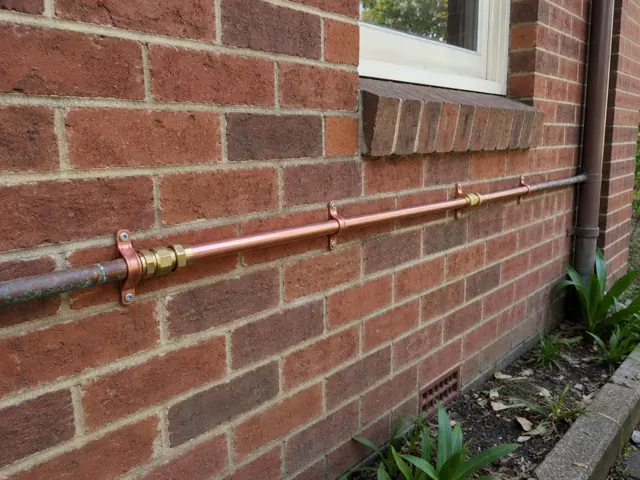 Copper water pipe fixed along an exterior brick wall beneath a window in Killara